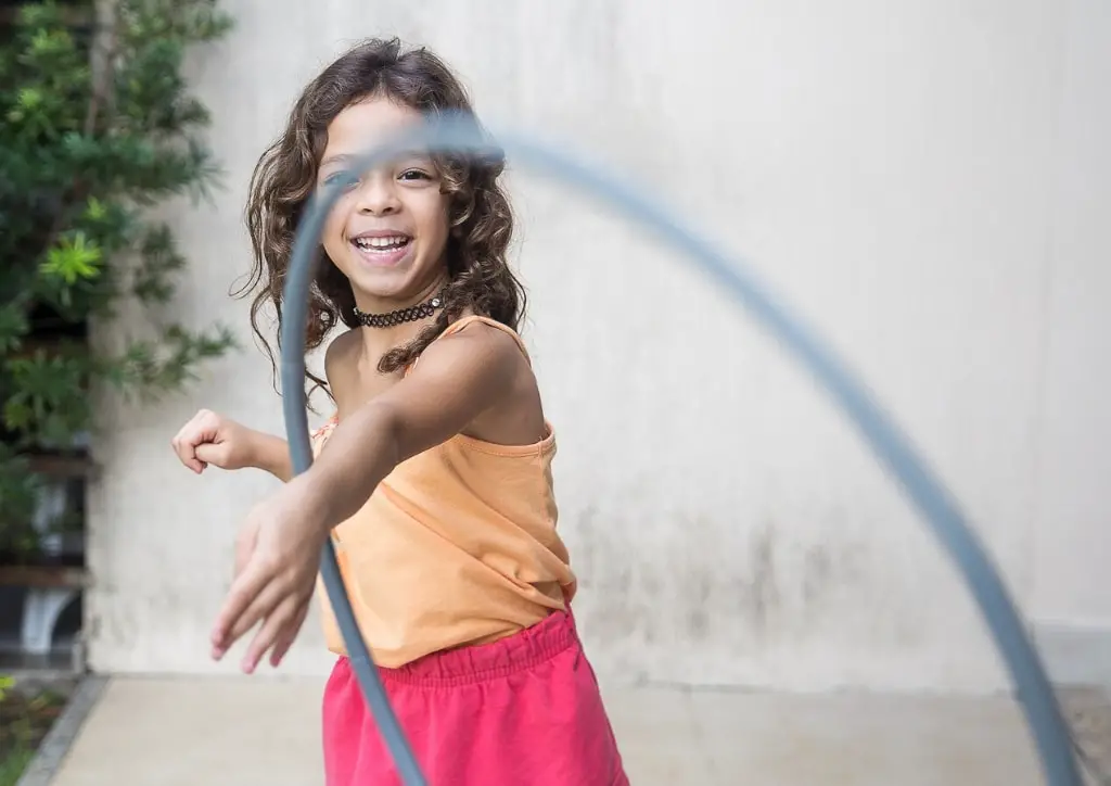 Petite fille jouant avec un cerceau au hula hop, un jeu de plein air qui se joue seul.